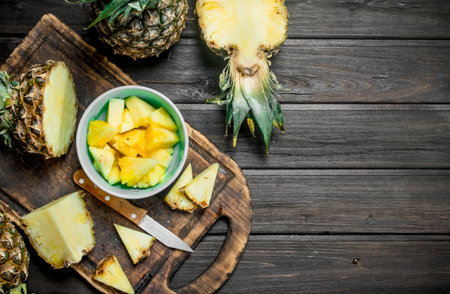 Cut a pineapple in a bowl and on a cutting Board with a knife. On wooden backgroundの写真素材