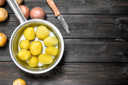 Peeled potatoes in a saucepan with a knife. On wooden backgroundの写真素材