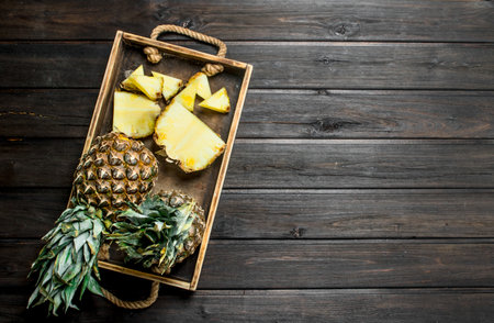 Whole and slices of ripe pineapple on a tray. On wooden backgroundの写真素材