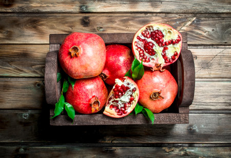 Ripe pomegranates with leaves in the box. On wooden backgroundの写真素材