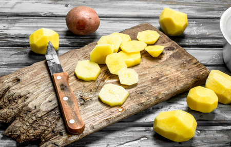 Pieces of fresh potatoes on a cutting Board with a knife. On wooden backgroundの写真素材
