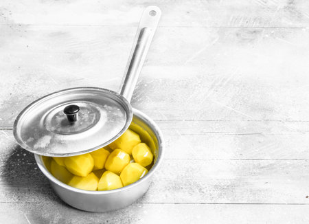Peeled potatoes in a sauce pan. On white rustic backgroundの写真素材