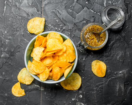 Potato chips in a bowl with mustard. On black rustic background.の写真素材