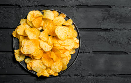 Potato chips on the plate. On black rustic background.の写真素材