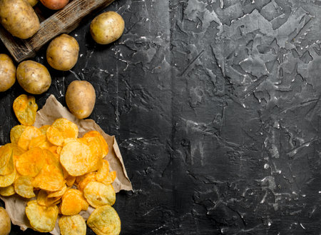 Potato chips on paper. On black rustic background.の写真素材