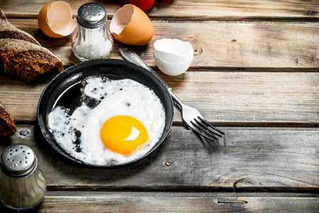Fried egg in a pan with rye bread. On a wooden background.の写真素材