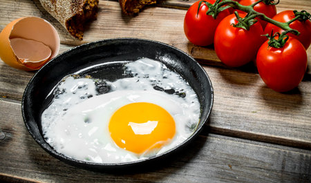 Fried egg in a pan with bread, tomatoes and green onions. On a wooden background.の写真素材