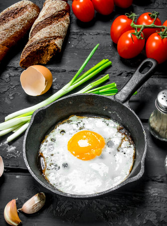 Fried egg in a pan with bread and tomatoes. On black rustic background.の写真素材