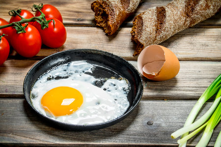 Fried egg in a pan with bread, tomatoes and green onions. On a wooden background.の写真素材