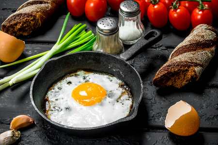 Fried egg in a pan with bread and tomatoes. On black rustic background.の写真素材