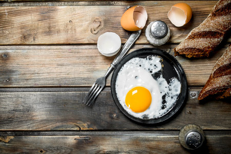 Fried egg in a pan with rye bread. On a wooden background.の写真素材