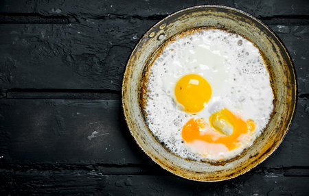 Fried eggs in a frying pan. On black rustic background.の写真素材