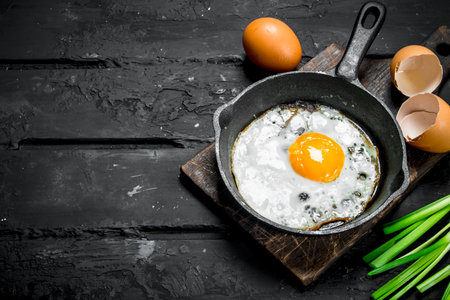 Fried egg with green onions and seasonings. On black rustic background.の写真素材