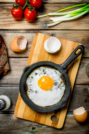 Fried egg in a pan with bread, tomatoes and green onions. On a wooden background.の写真素材
