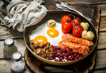 English breakfast. Fried eggs with sausages, bacon and red canned beans. On a wooden background.の写真素材