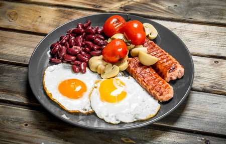 English breakfast. Fried eggs with sausages, mushrooms and beans. On a wooden background.の写真素材