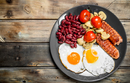 English breakfast. Fried eggs with sausages, mushrooms and beans. On a wooden background.の写真素材