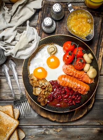 English breakfast. Fried eggs with sausages, bacon and red canned beans. On a wooden background.の写真素材
