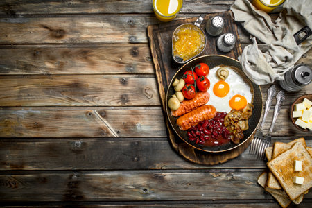 English breakfast. Fried eggs with sausages, bacon and red canned beans. On a wooden background.の写真素材