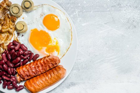 English breakfast. Fried eggs with sausages, bacon and beans. On a rustic background.の写真素材