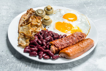 English breakfast. Fried eggs with sausages, bacon and beans. On a rustic background.の写真素材