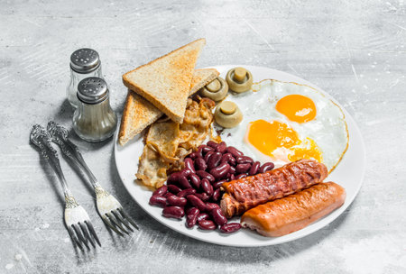 English breakfast. Fried eggs with sausages, bacon and beans. On a rustic background.の写真素材