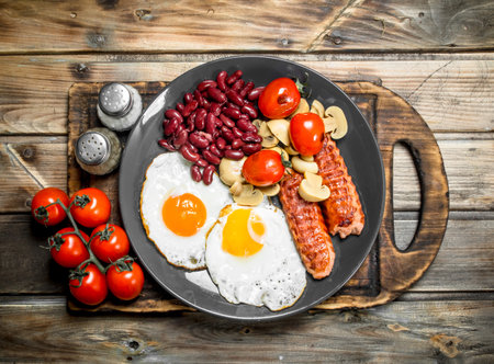 English breakfast. Fried eggs with sausages, mushrooms and beans. On a wooden background.の写真素材