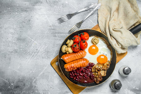 English breakfast. Fried eggs with sausages, bacon and beans. On a rustic background.の写真素材