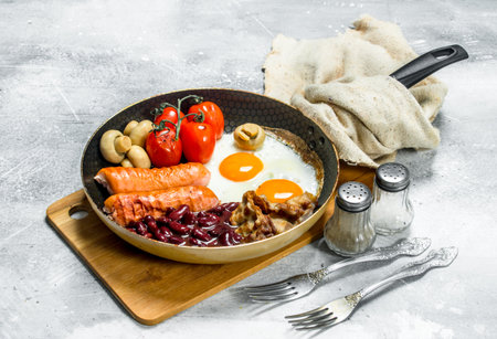 English breakfast. Fried eggs with sausages, bacon and beans. On a rustic background.の写真素材
