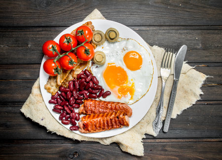 Traditional English Breakfast with fried eggs, sausages and beans. On a wooden background.の写真素材