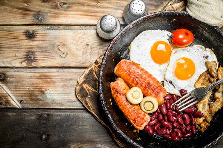 English breakfast. Fried eggs with tomatoes, sausages and beans. On a wooden background.の写真素材