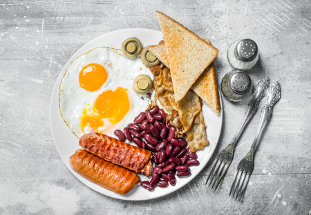 English breakfast. Fried eggs with sausages, bacon and beans. On a rustic background.の写真素材