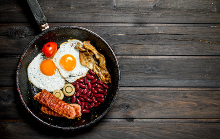 Traditional English Breakfast with fried eggs, sausages and beans. On a wooden background.の写真素材