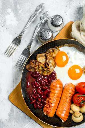 English breakfast. Fried eggs with sausages, bacon and beans. On a rustic background.の写真素材