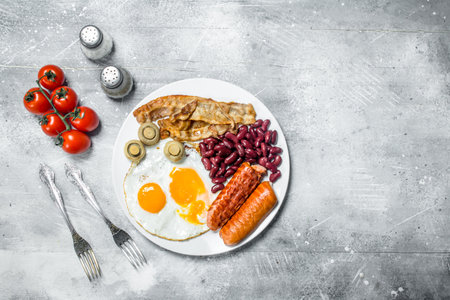 English breakfast. Fried eggs with sausages, bacon and beans. On a rustic background.の写真素材