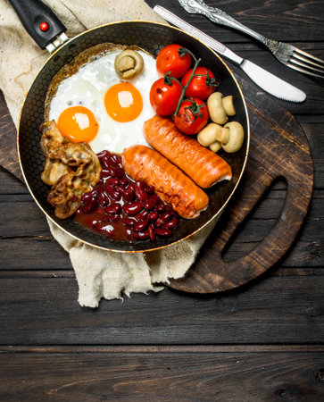 Traditional English Breakfast with fried eggs, sausages and beans. On a wooden background.の写真素材