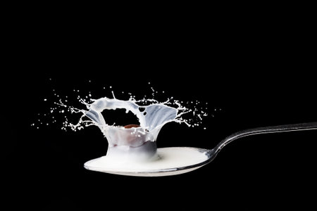 Metal spoon full of milk with high speed splash. On black backgroundの写真素材