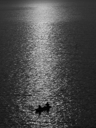 black and white silhouette man fishing in the sea with light sunsetの写真素材