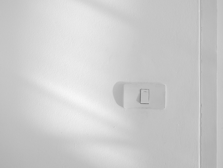 light switch on white wall in the room with light and shadow