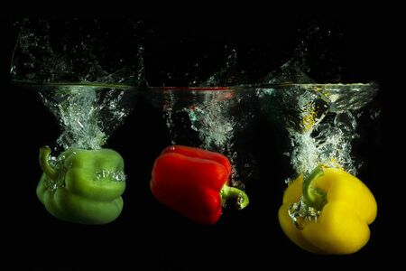 Green, red and yellow peppers splashing in clear water with a black background.  の写真素材