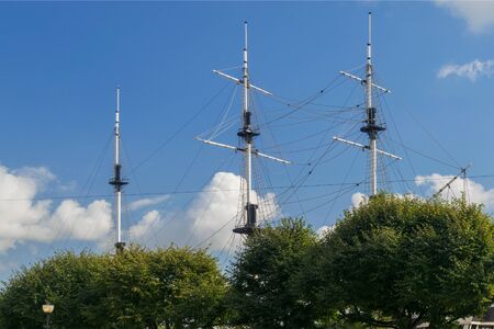 The mast of the ship behind the trees against the clear sky