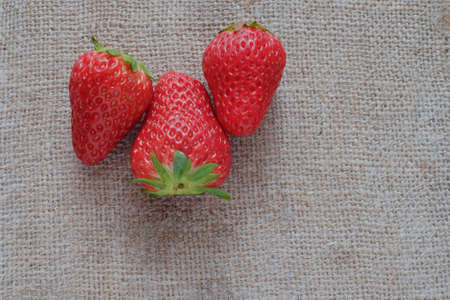 Three ripe juicy strawberries on a background of rough burlap cloth.の写真素材