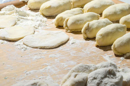 Dough on a Board with flour and pies. Cooking homemade hotcakes with onion and egg filling....