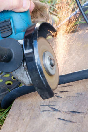 Sparks fly out from under the disc of the manual circular abrasive saw when cutting the...