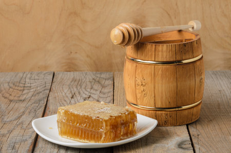 Honey in honeycomb on a white plate with a wooden jar and spoon on a rough wooden background. Selective focus.の写真素材