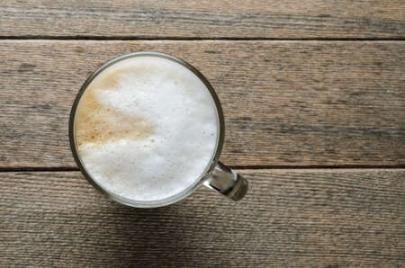 Top view of a cappuccino coffee mug with a foam of whipped cream on a background of wooden boards.の写真素材
