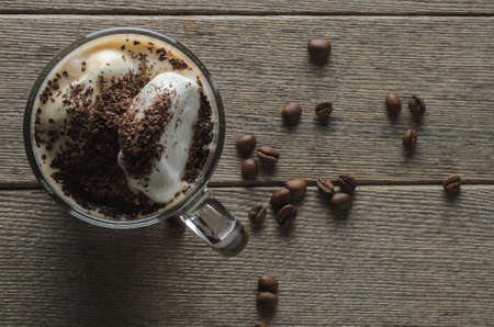 Glass cup of coffee with milk, ice cream and grated chocolate on a wooden surface with roasted...