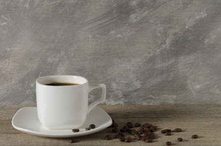 A mug of coffee on a wooden table with scattered roasted beans. Selective focus.