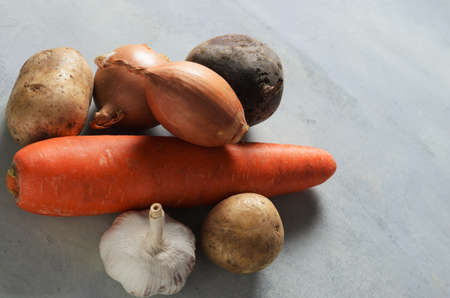 Garlic, onion, carrot, beetroot, potato vegetables on a textured yellow-gray background.