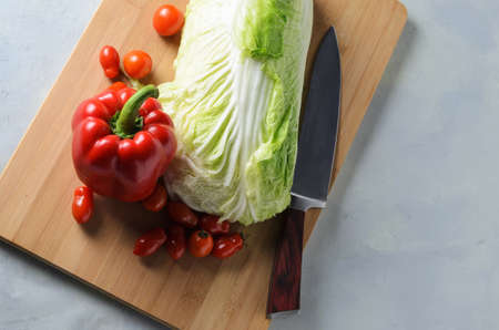 Vegetables on a chopping board. Red bell pepper, tomatoes, Peking cabbage, chopping knife on the board. Selective focus.の写真素材